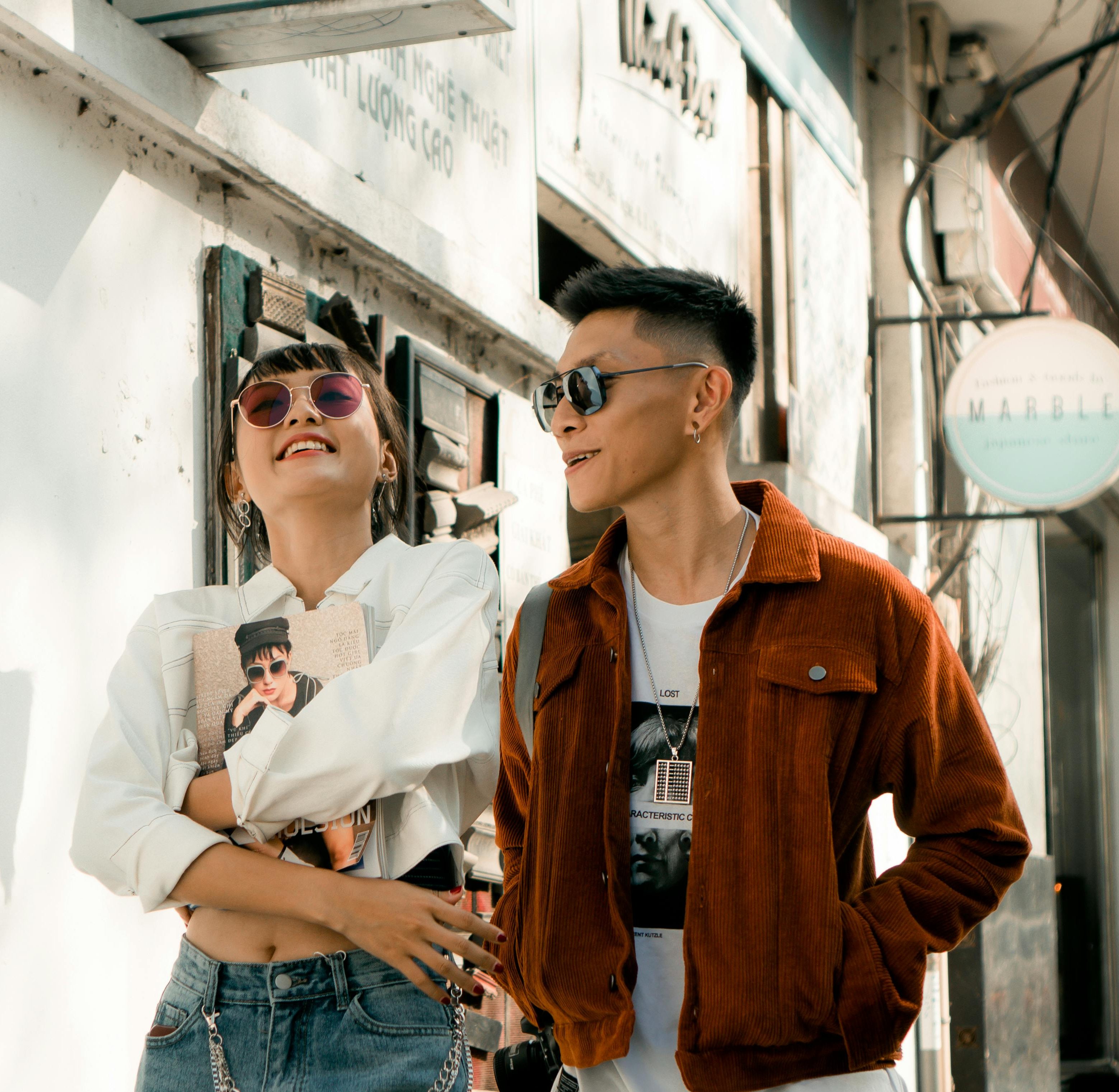 A fashion-forward couple enjoys a sunny walk in stylish outfits, exuding happiness and urban flair.