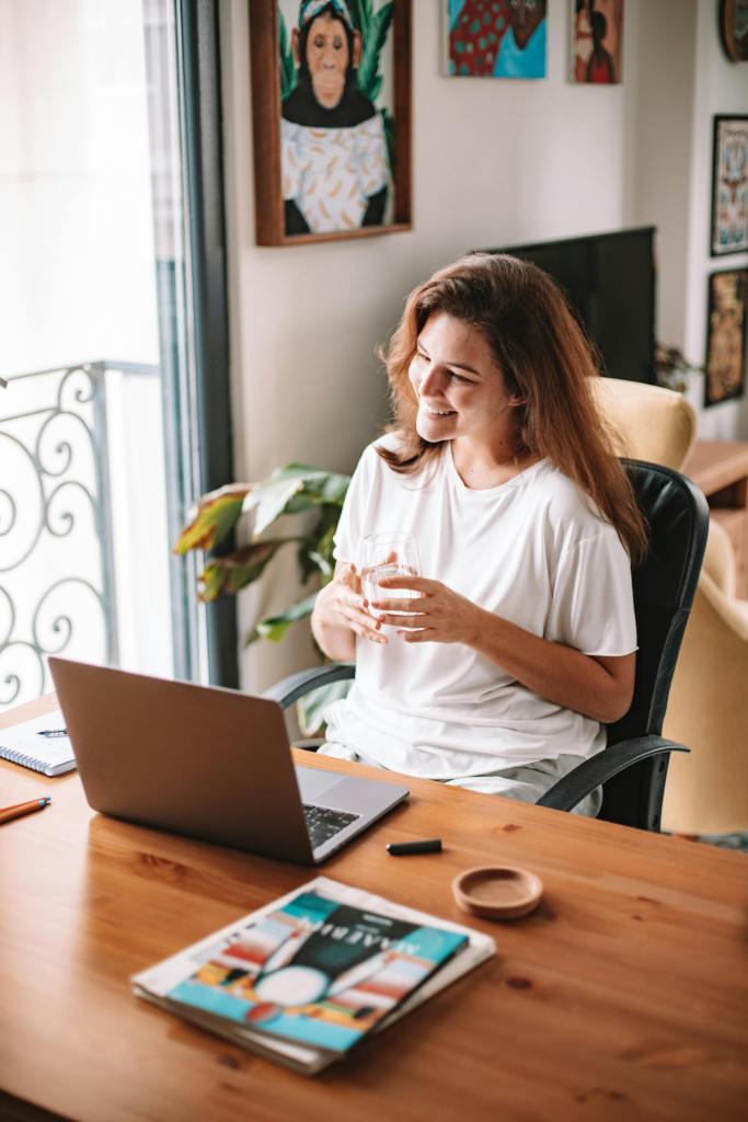 Smiling woman at desk with laptop, enjoying a coffee in a cozy home office.