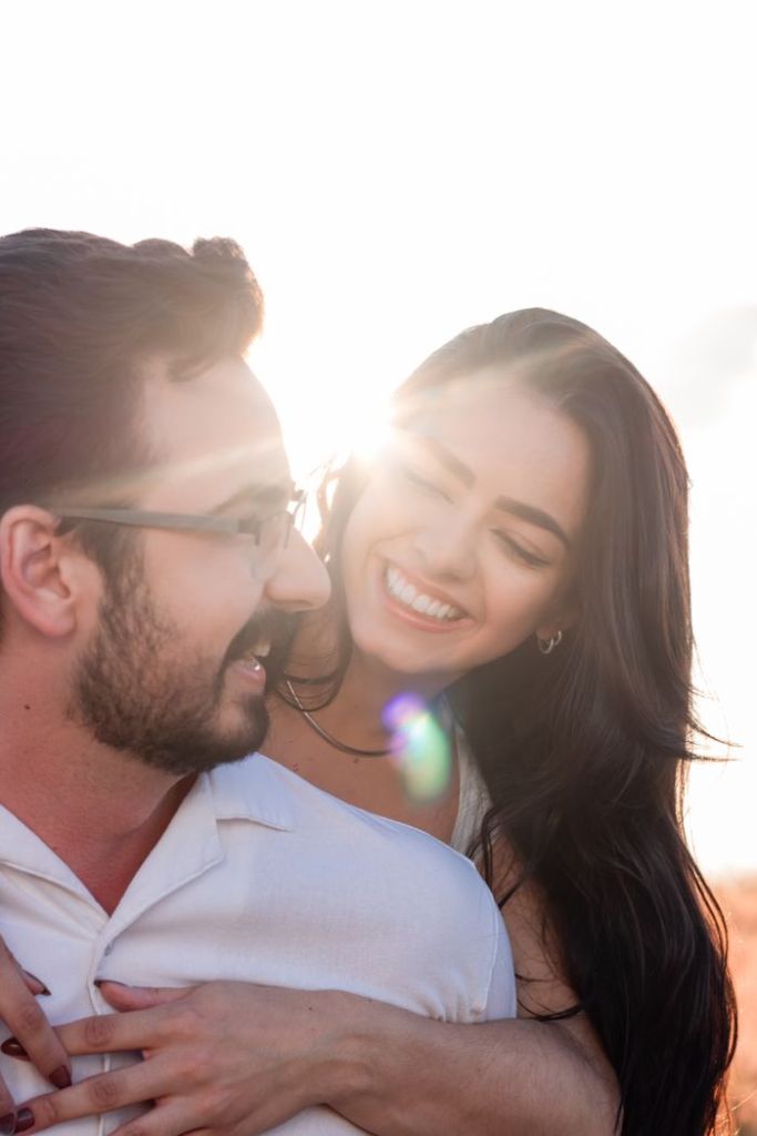 Happy couple embracing at sunset, smiling joyfully against a bright sky.