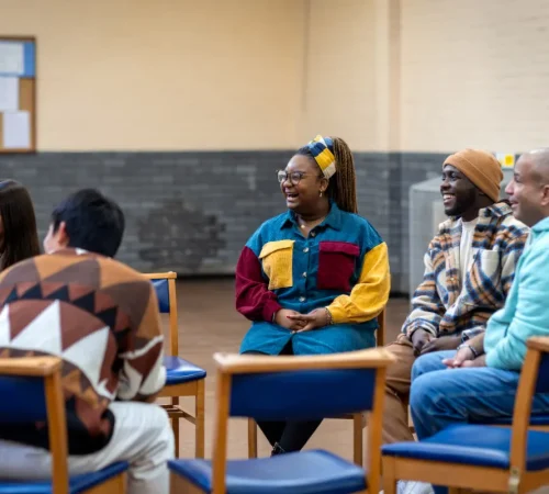 A diverse group of people sitting in a circle in a community room, engaged in a group discussion.