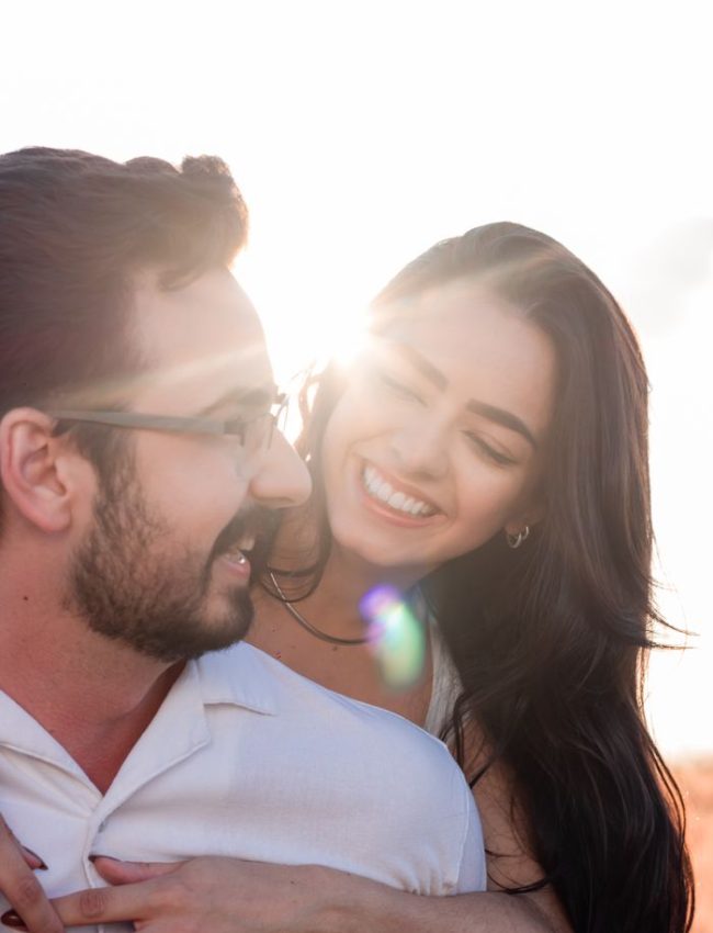 Happy couple embracing at sunset, smiling joyfully against a bright sky.